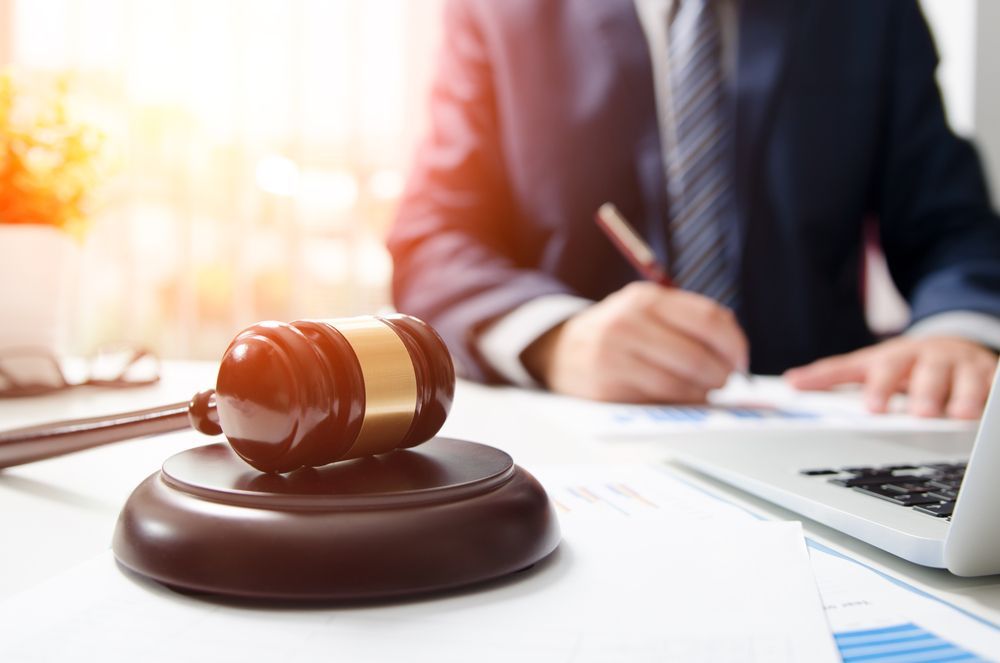 Gavel on a Desk; a Person in a Suit is Writing, With a Laptop Nearby — Umbrella Legal in Maitland, NSW