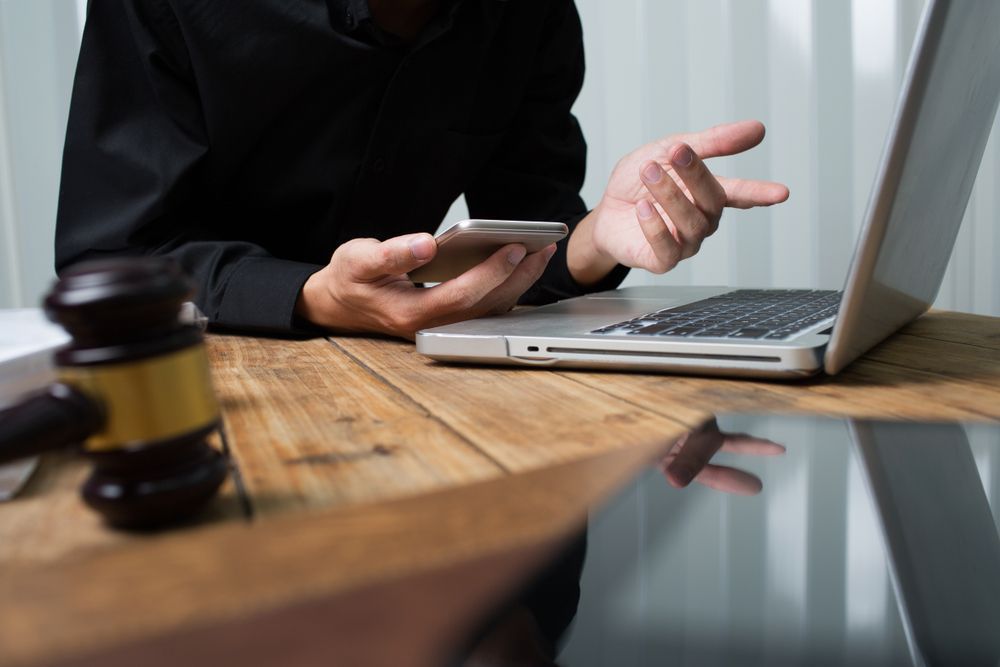 Person With Phone and Laptop at Desk, Gavel in the Foreground — Umbrella Legal in Wyong, NSW