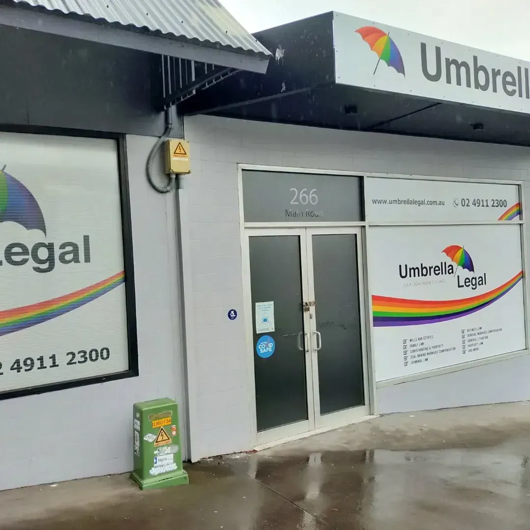 Rainy street view of a Umbrella Legal office entrance with white signage and glass doors