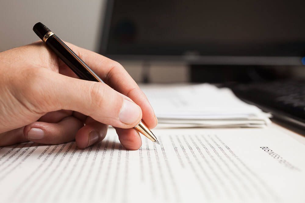 Hand Holding a Pen, Writing on a Stack of Papers — Umbrella Legal in Cardiff, NSW
