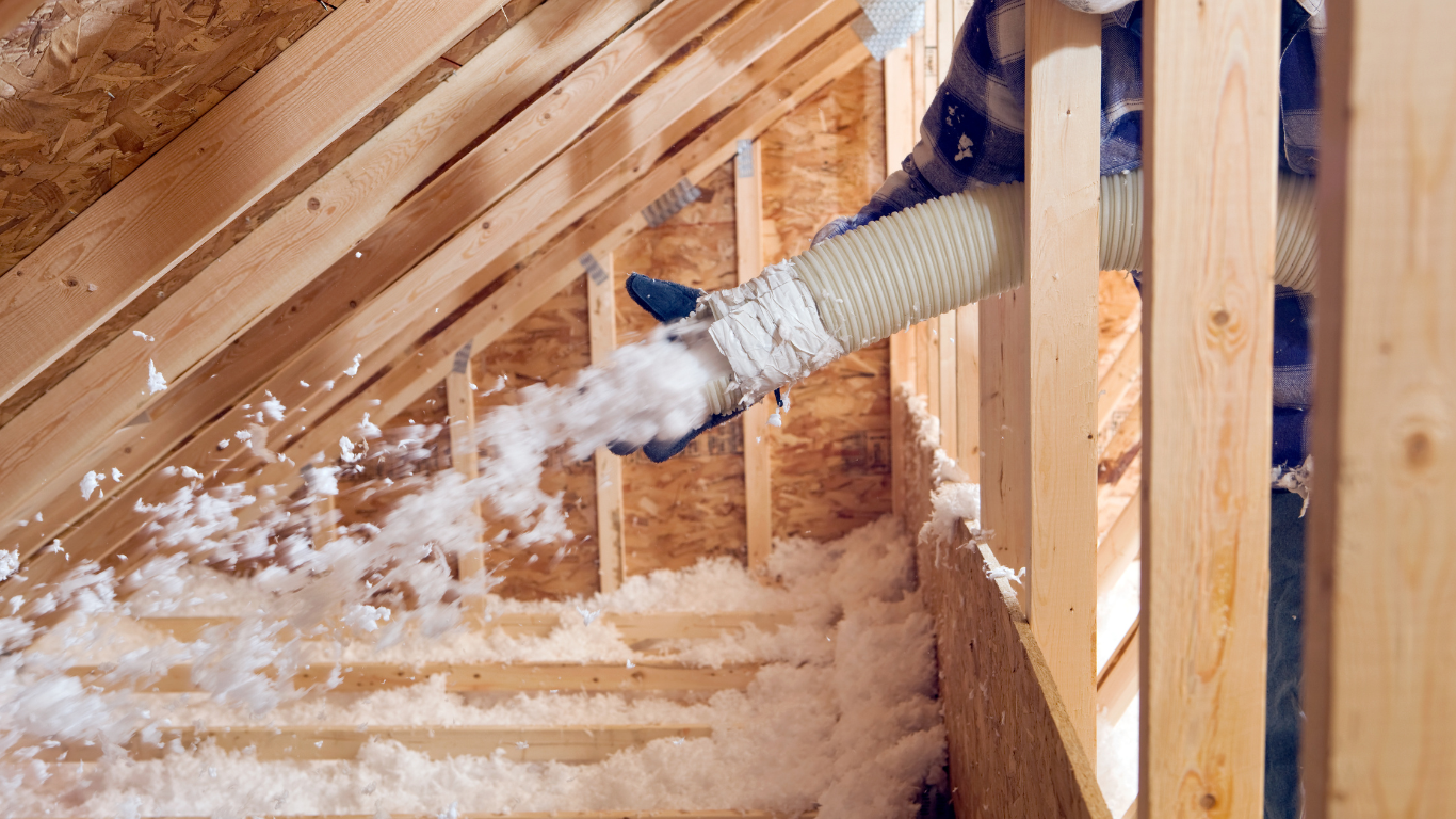 A man is blowing insulation into the attic of a house under construction.