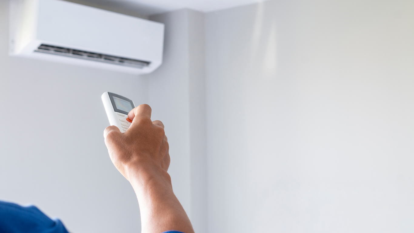 A person is holding a remote control in front of an air conditioner.