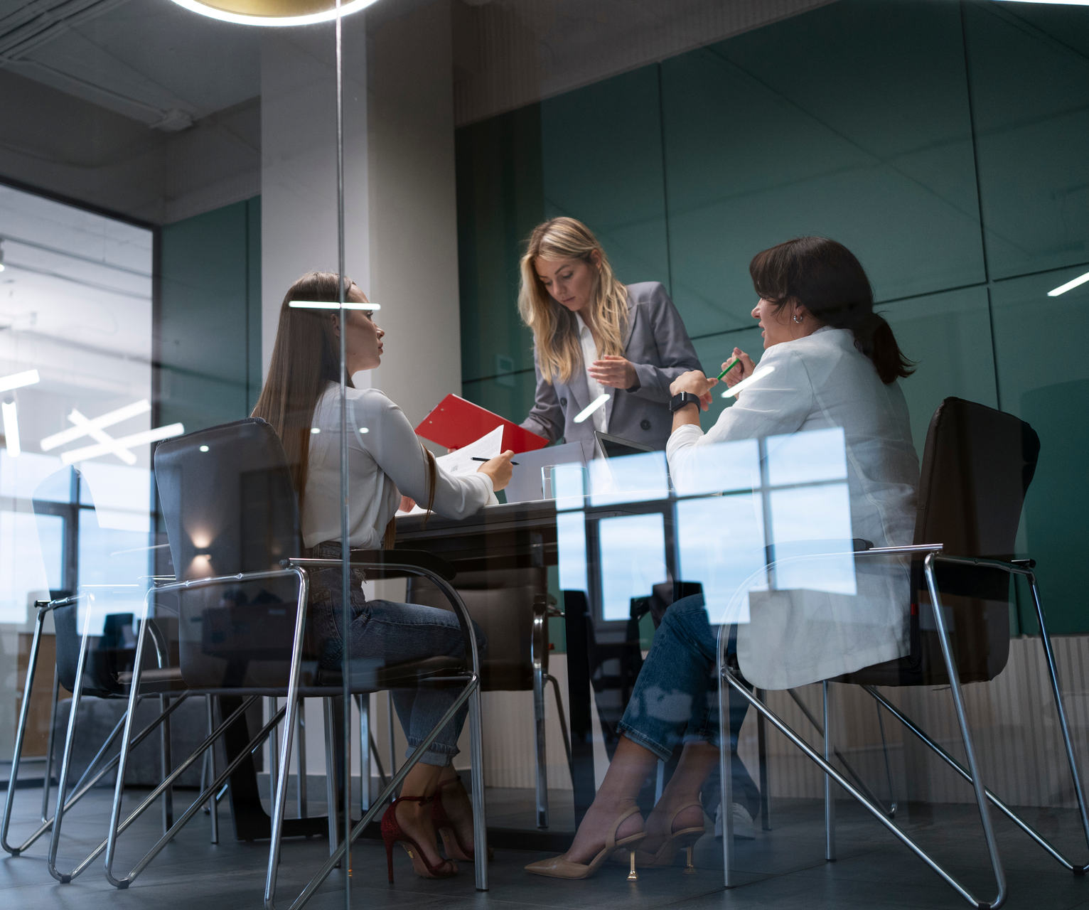 Three people in a glass conference room reviewing papers around a table