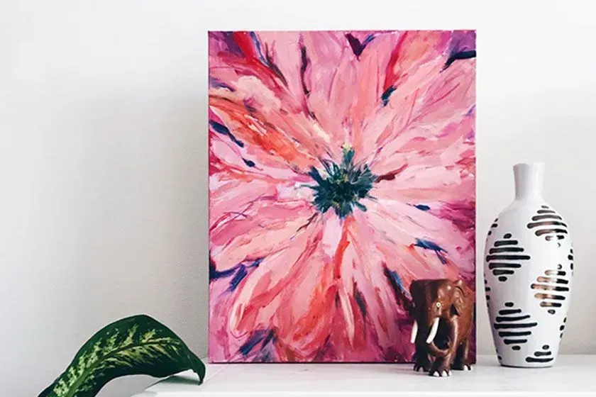 A painting of a pink flower is sitting on a shelf next to two vases.