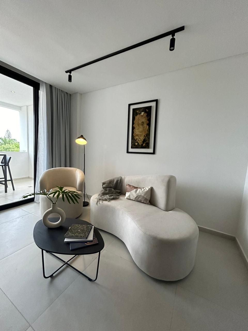 Una sala de estar con un sofá y una silla curvados de colores claros, una mesa de café negra y obras de arte