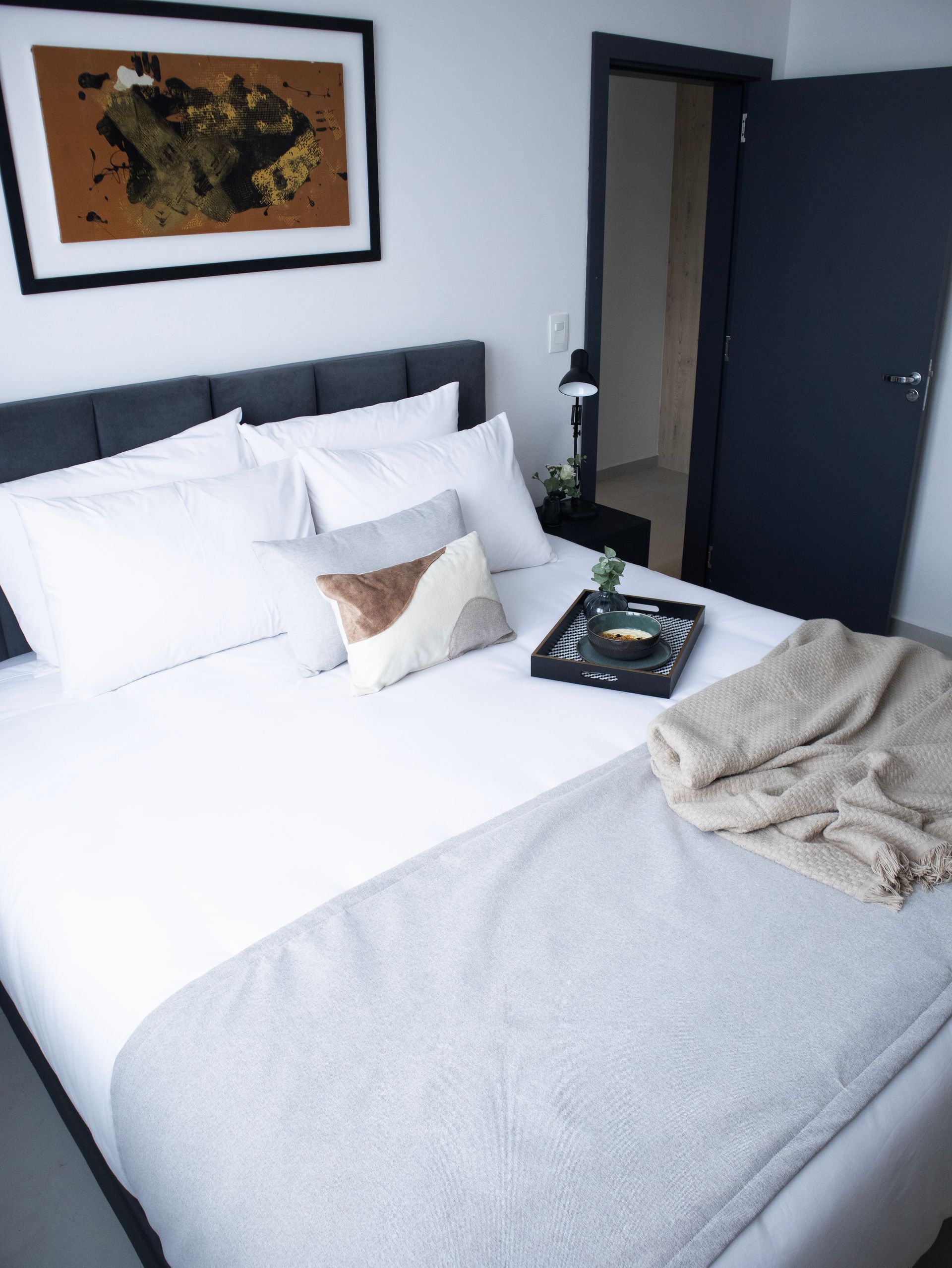 Dormitorio con cama, almohadas, manta, arte y puerta abierta.