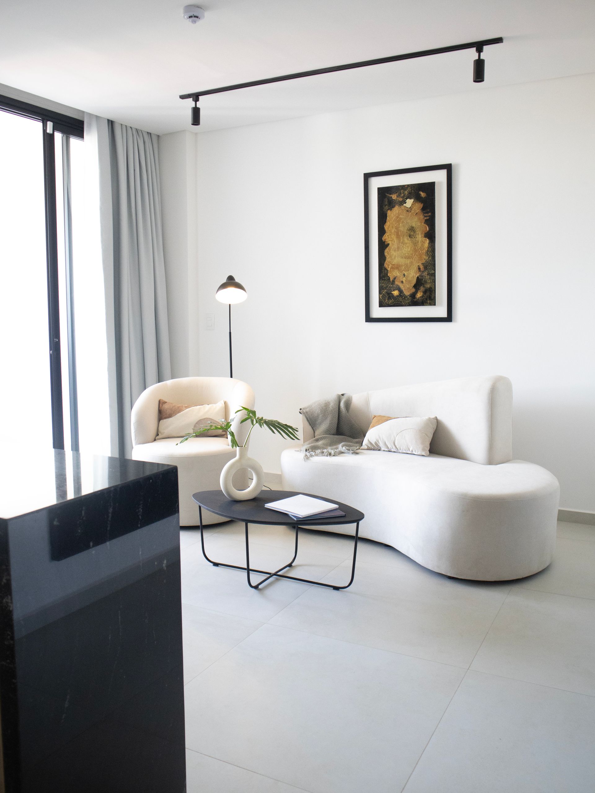 Sala de estar moderna con sofá curvo blanco, silla, mesa de café y arte.