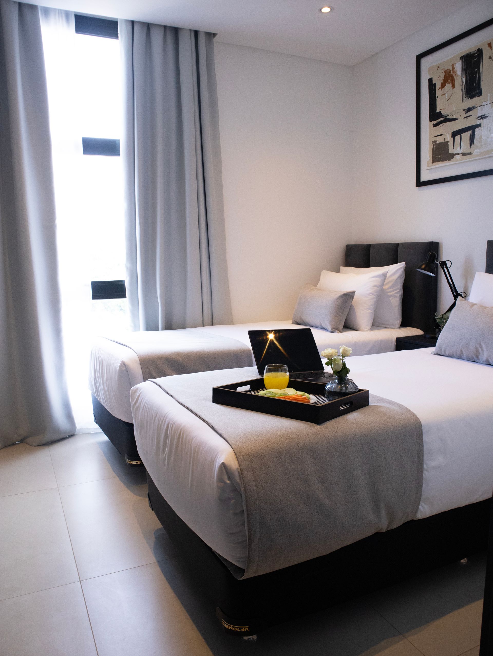 Dos camas individuales en una habitación moderna, ropa de cama gris, una bandeja con bocadillos