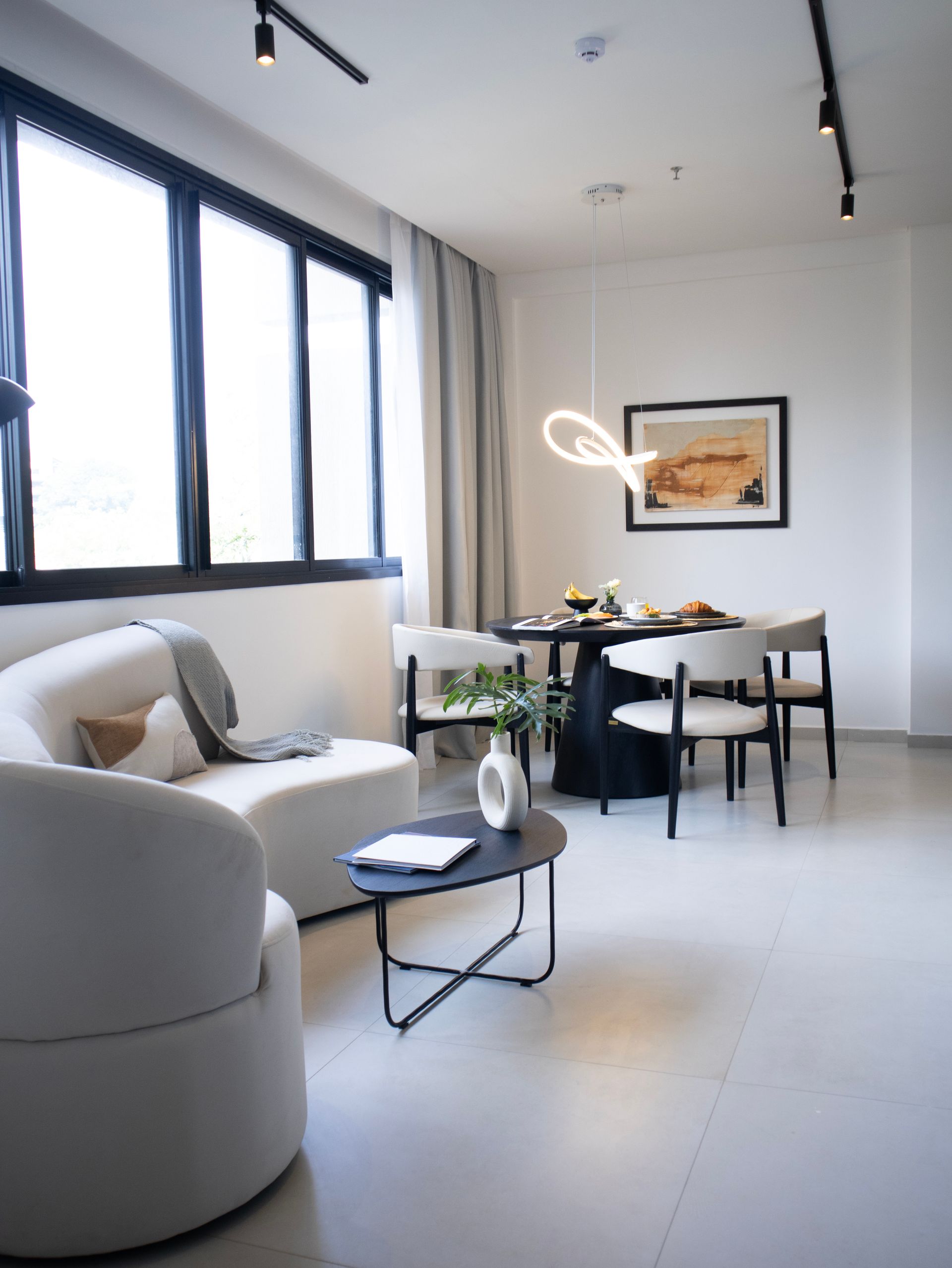 Moderna sala de estar con sofá blanco, mesa redonda negra, comedor y gran ventanal.