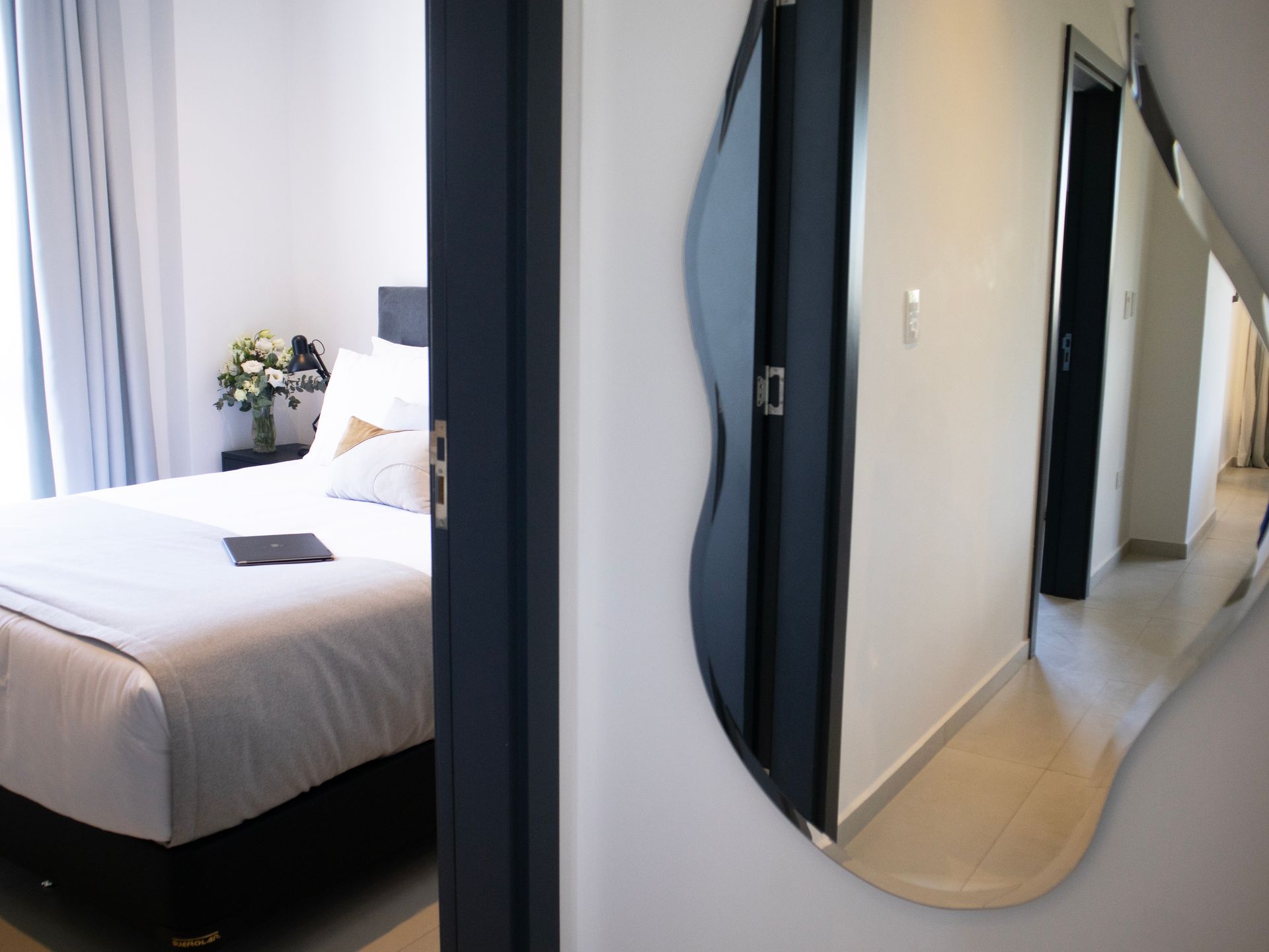 Dormitorio con un vistazo a una cama, un espejo con una forma de onda única y un pasillo.