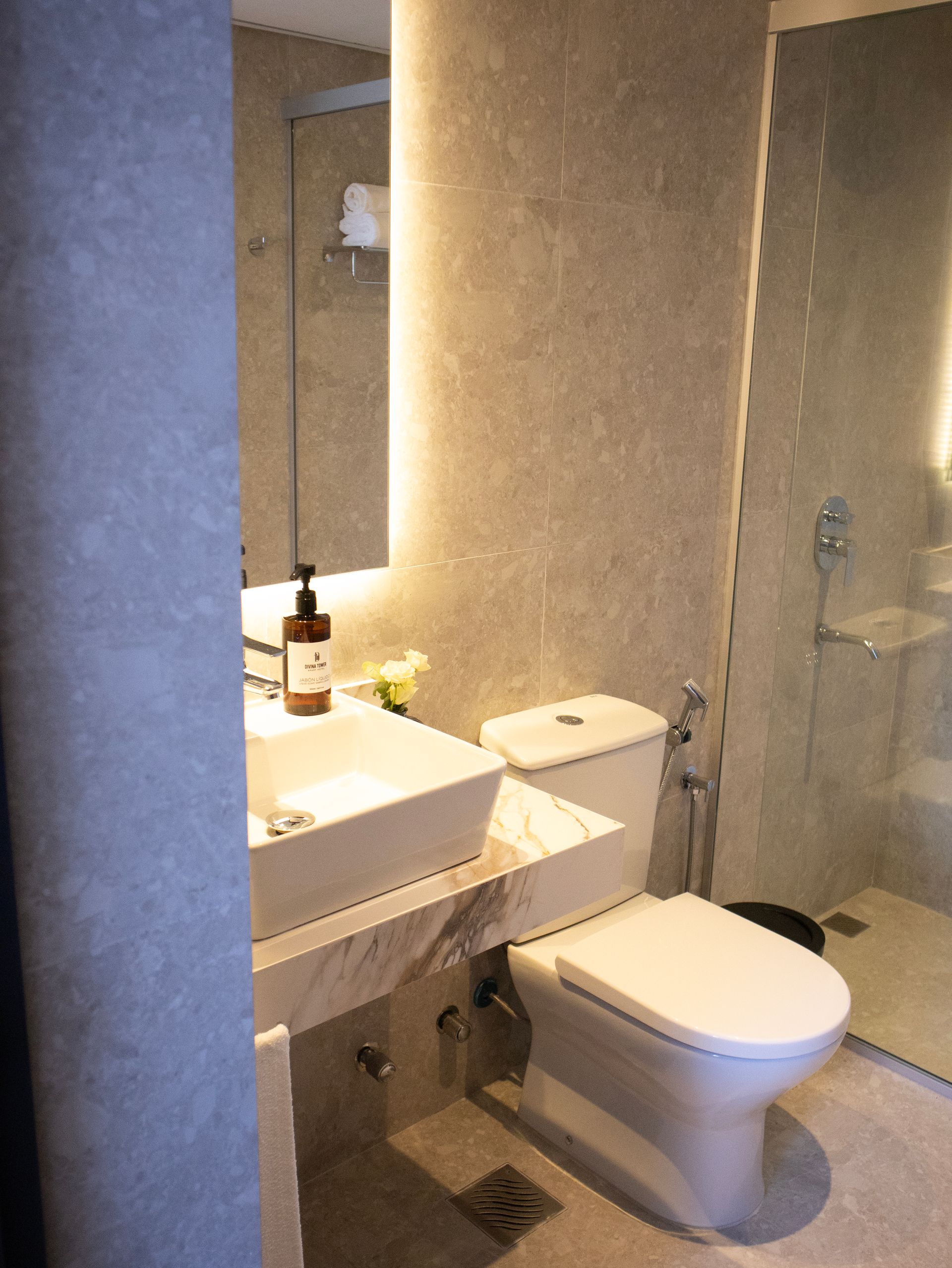 Baño moderno con inodoro blanco, lavabo y ducha detrás de un cristal.