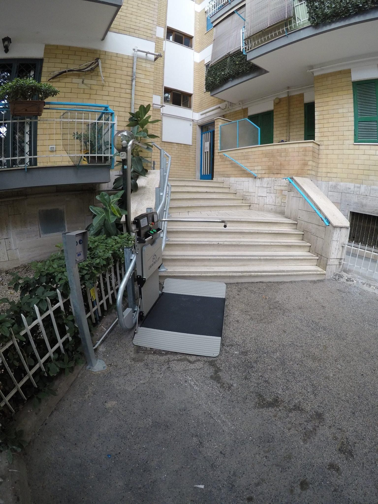 Un montascale per sedie a rotelle accanto alle scale esterne di un edificio in mattoni gialli.