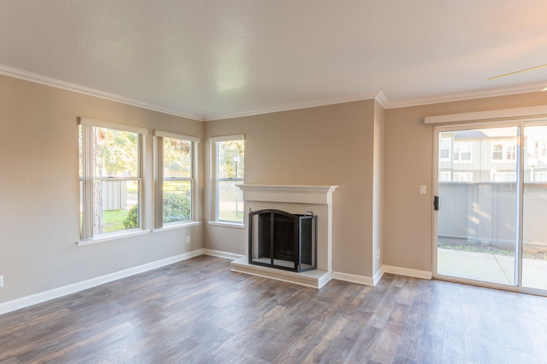 Bright living room with a fireplace, wood-look flooring, and a sliding glass door to a patio at Seventeen Mile Drive Village apartments in Pacific Grove, CA.