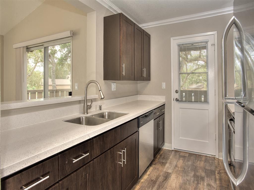 Modern apartment kitchen with dark wood cabinets, white countertops, and stainless appliances at Seventeen Mile Drive Village apartments in Pacific Grove, CA.