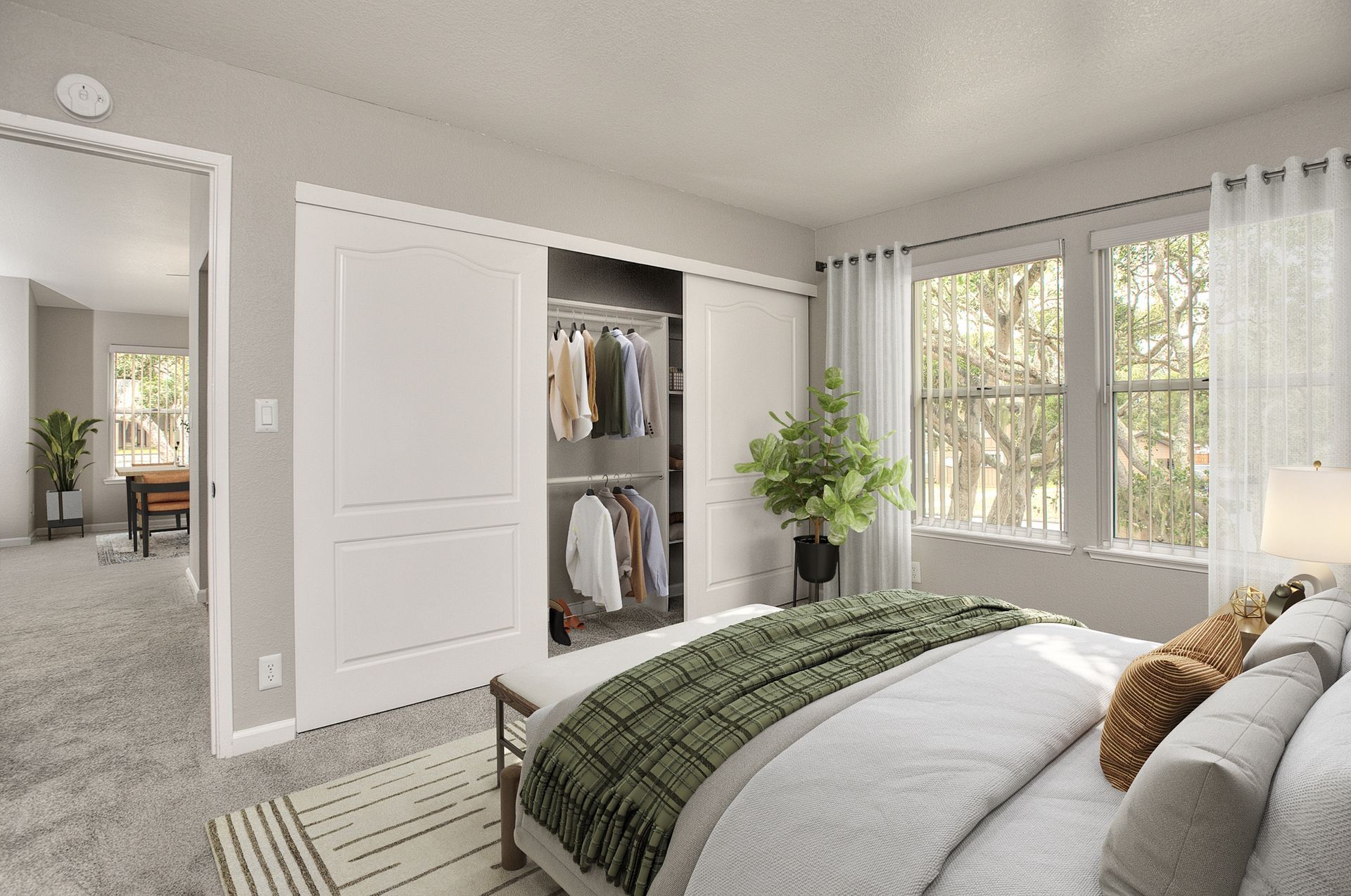 Bedroom with sliding closet doors, clothes hanging, a plant, and large windows at Seventeen Mile Drive Village apartments in Pacific Grove, CA.