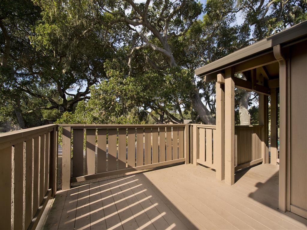 Wooden balcony deck with railing and trees beyond at Seventeen Mile Drive Village apartments in Pacific Grove, CA.
