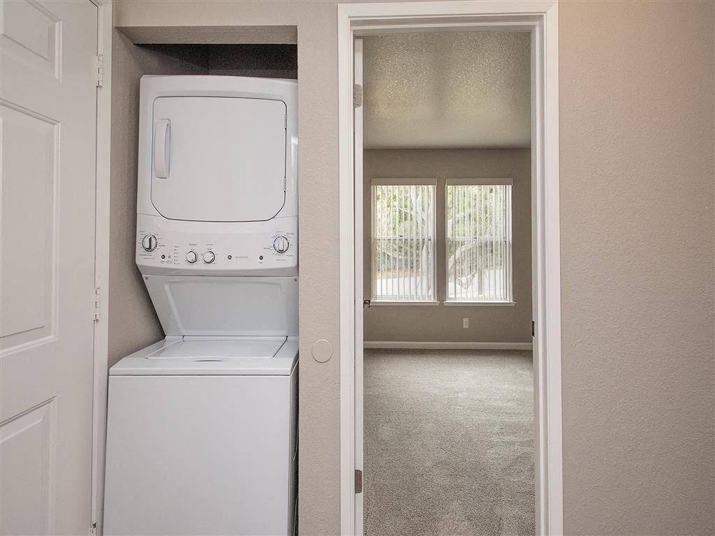 Stacked washer and dryer in a closet beside a doorway to a carpeted living area at Seventeen Mile Drive Village apartments in Pacific Grove, CA.