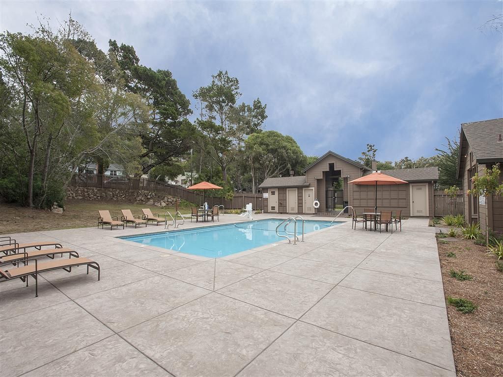 Outdoor community pool area with lounge chairs and umbrellas at Seventeen Mile Drive Village apartments in Pacific Grove, CA.