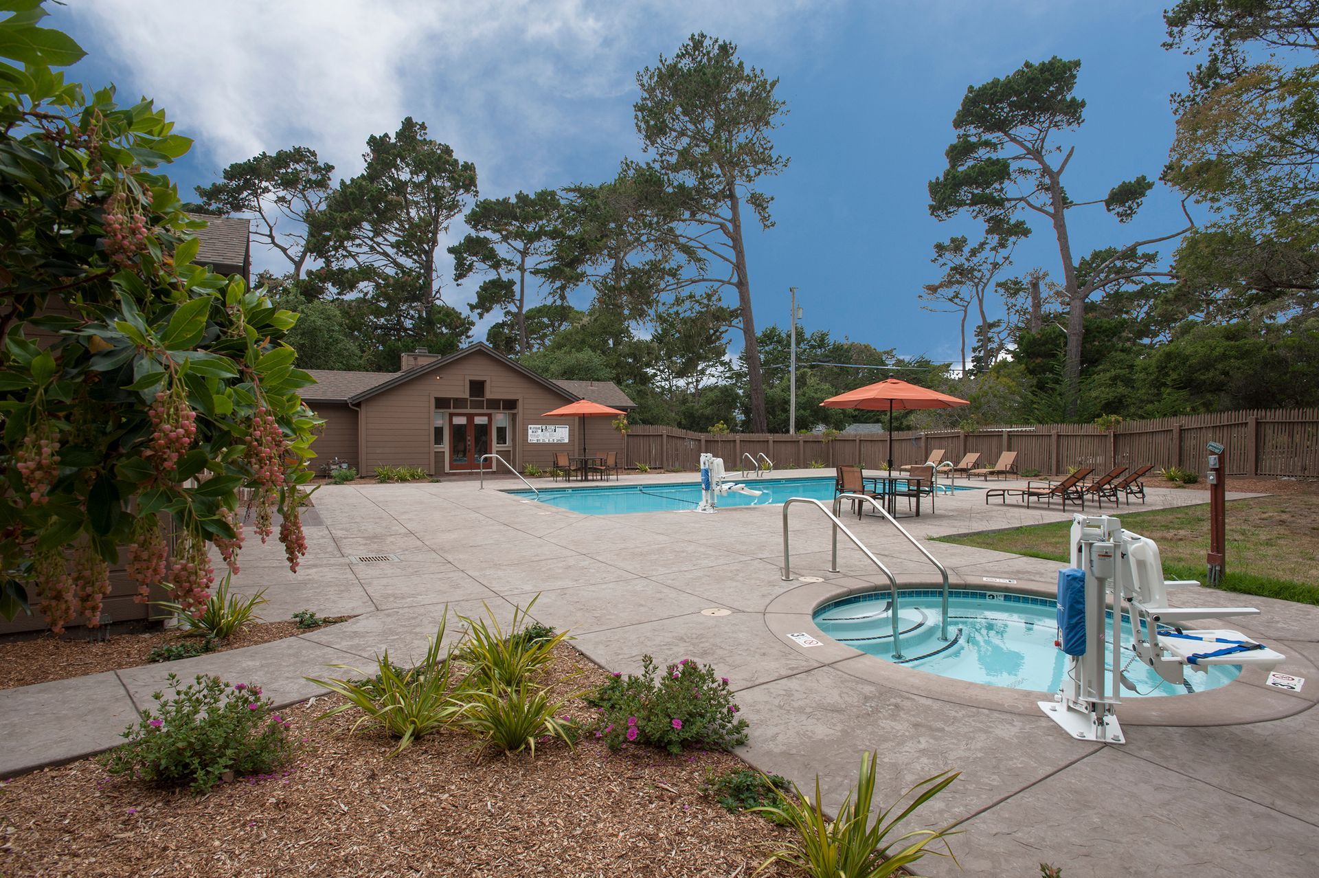 Outdoor pool area at a multifamily community with seating, umbrellas, and a pool house at Seventeen Mile Drive Village apartments in Pacific Grove, CA.