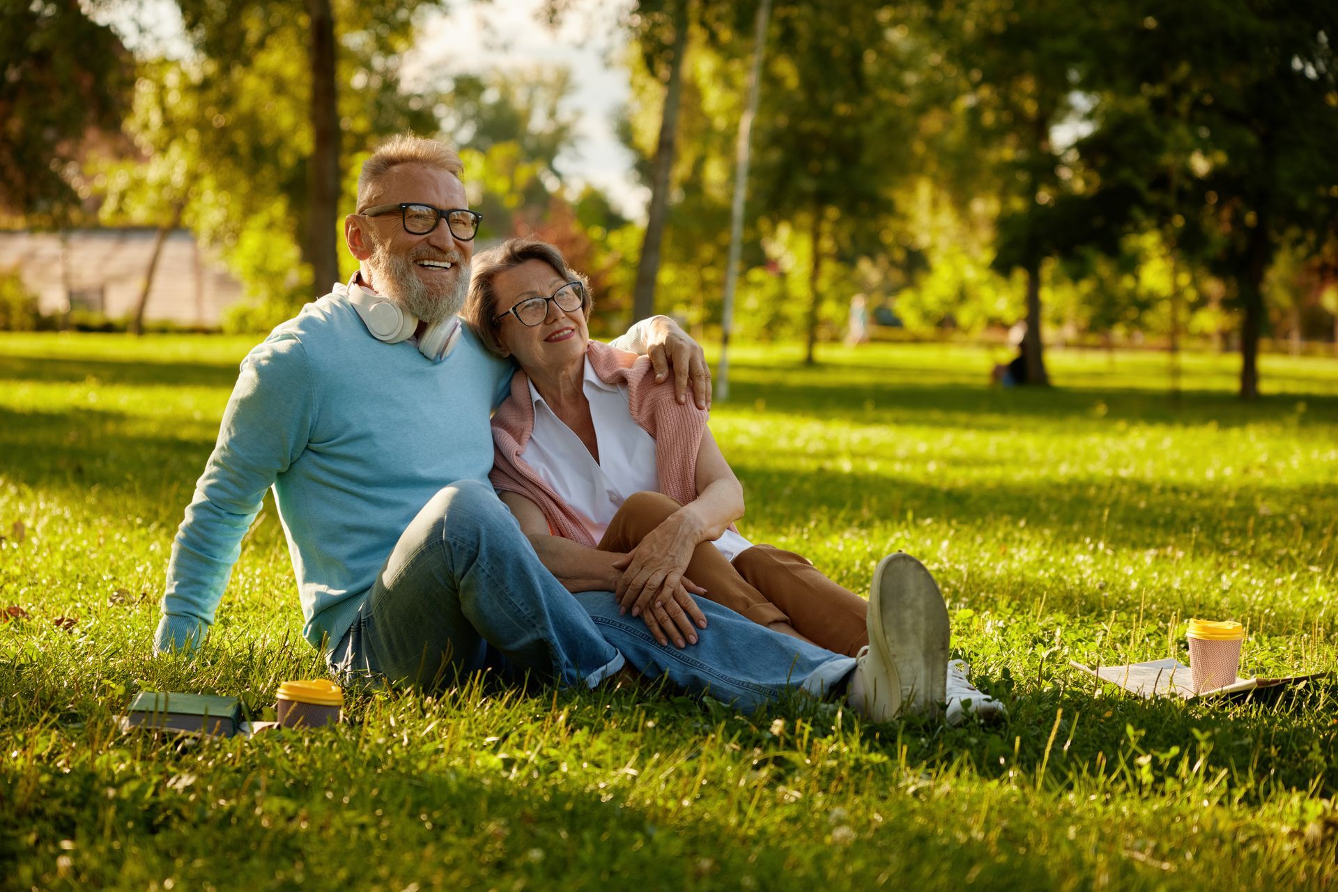 Couple sitting on grass in a park, man with arm around woman, smiling, sunny day.