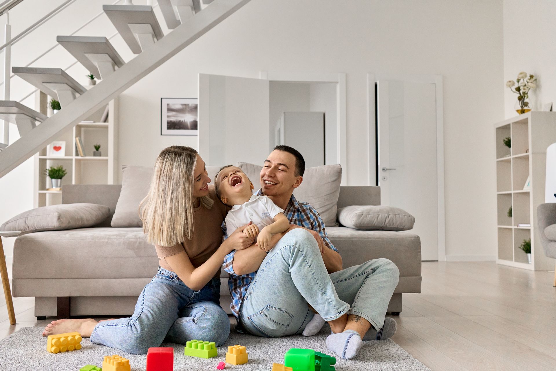 Parents playing with a child on the floor of a living room. They are laughing.