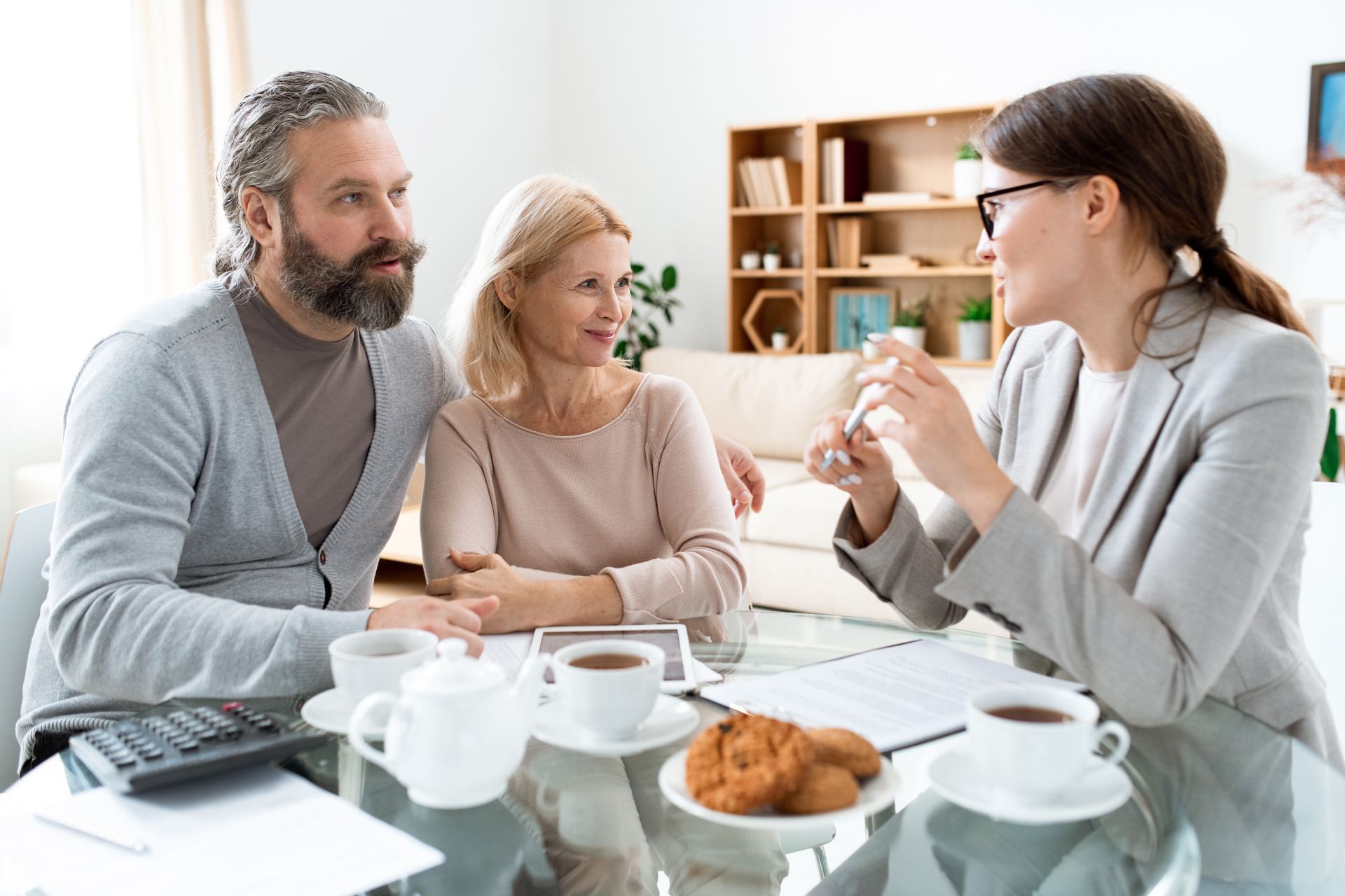 Couple consulting with a professional, seated at a table with papers, cups, and cookies.