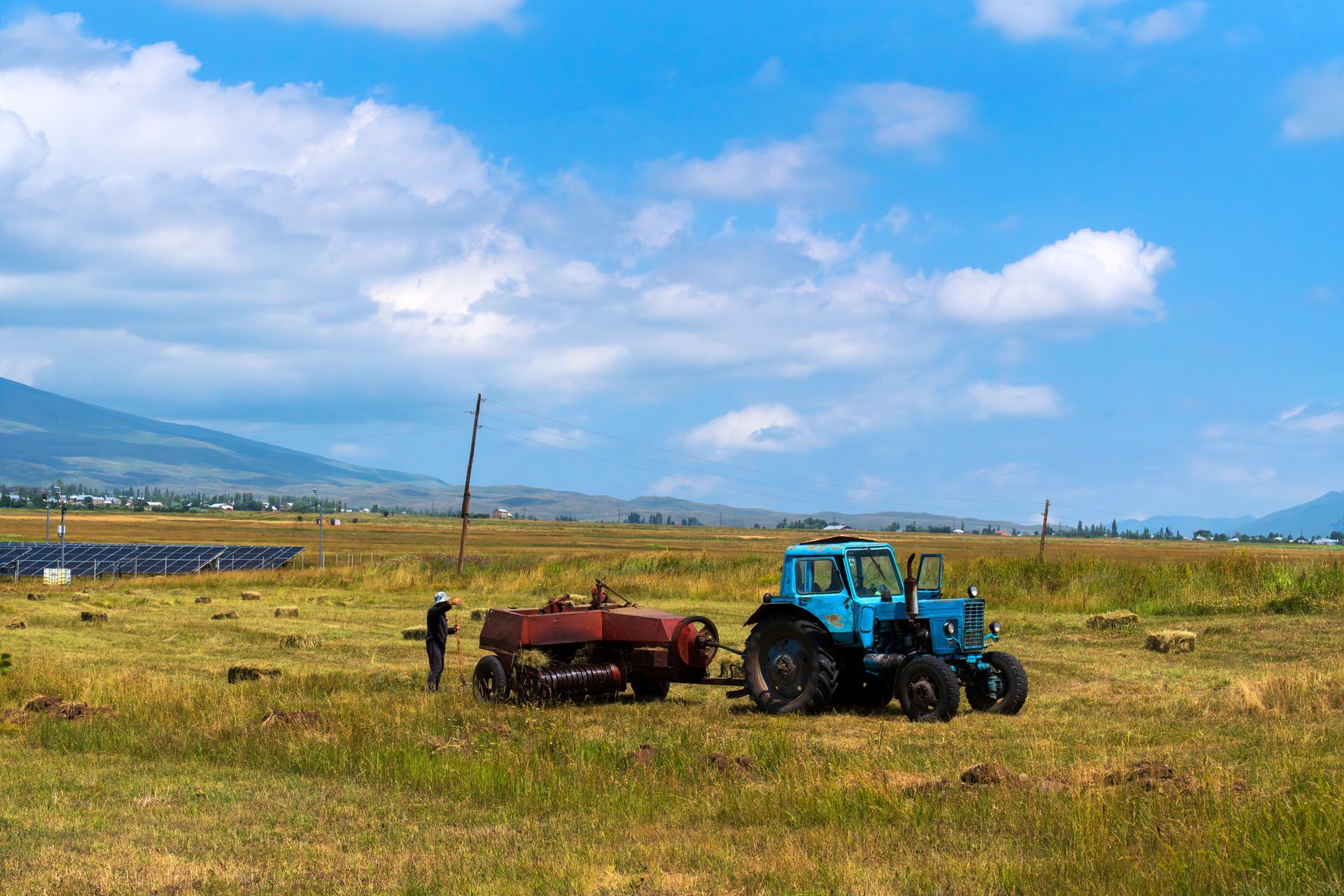 Blue tractor and farm worker in a field; mountains and blue sky in the background.