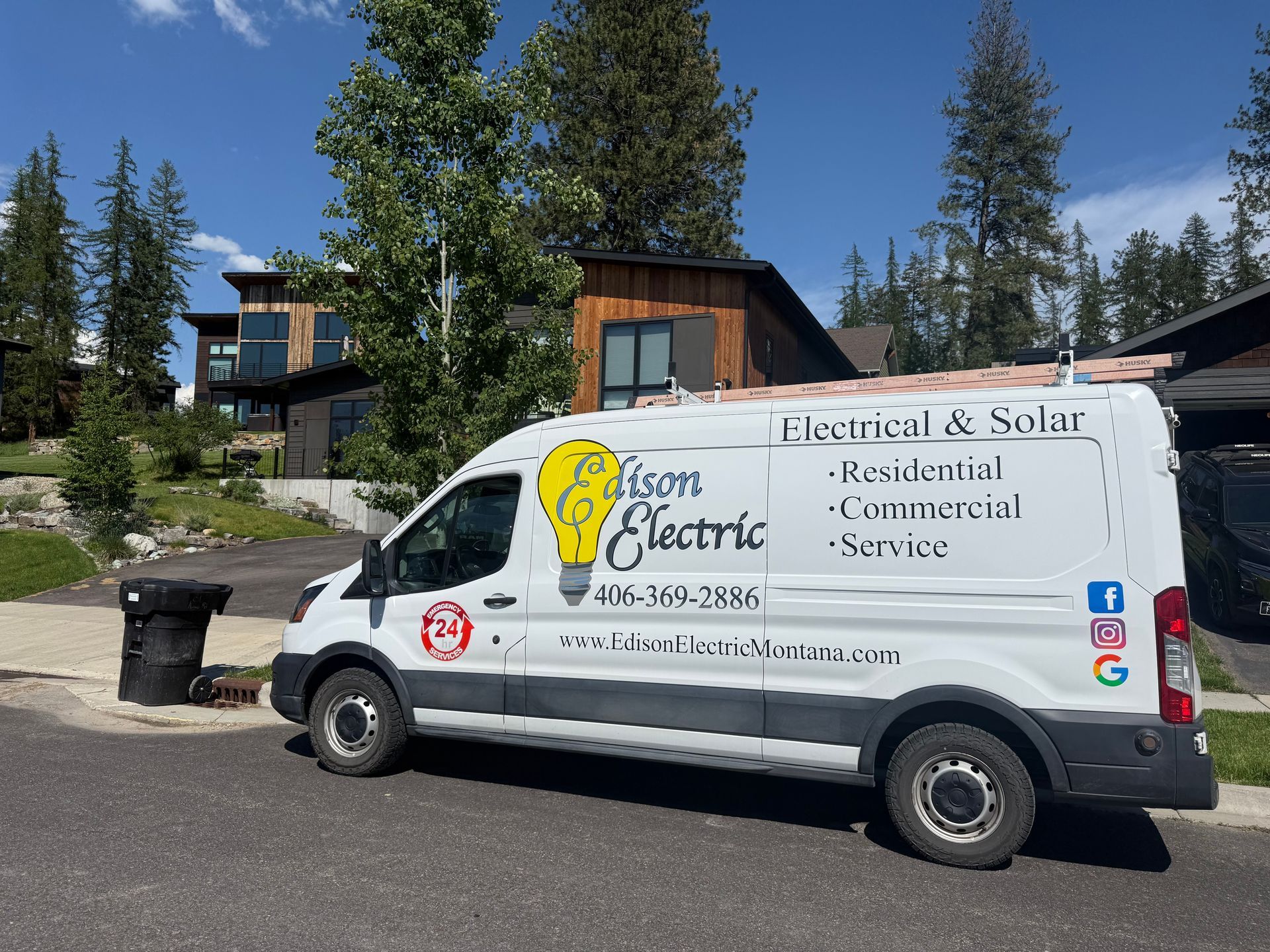 White solar/electrical service van parked outside two modern homes in a wooded area.