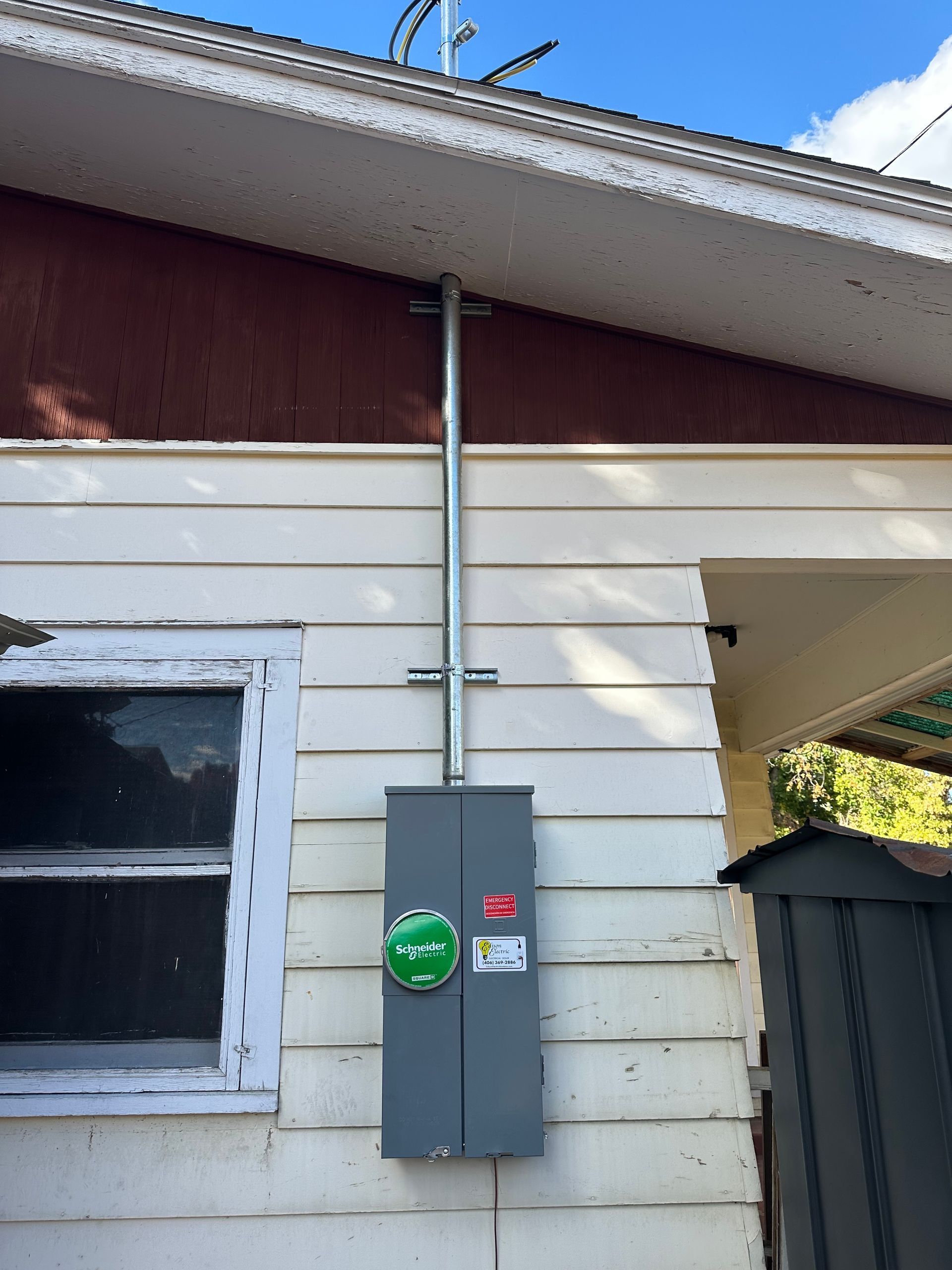 Gray electrical meter box and conduit mounted on the side of a white house beneath a roofline