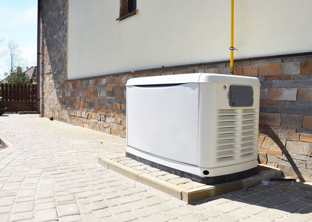 White outdoor generator beside a building on a paved driveway, with brick and stucco walls.