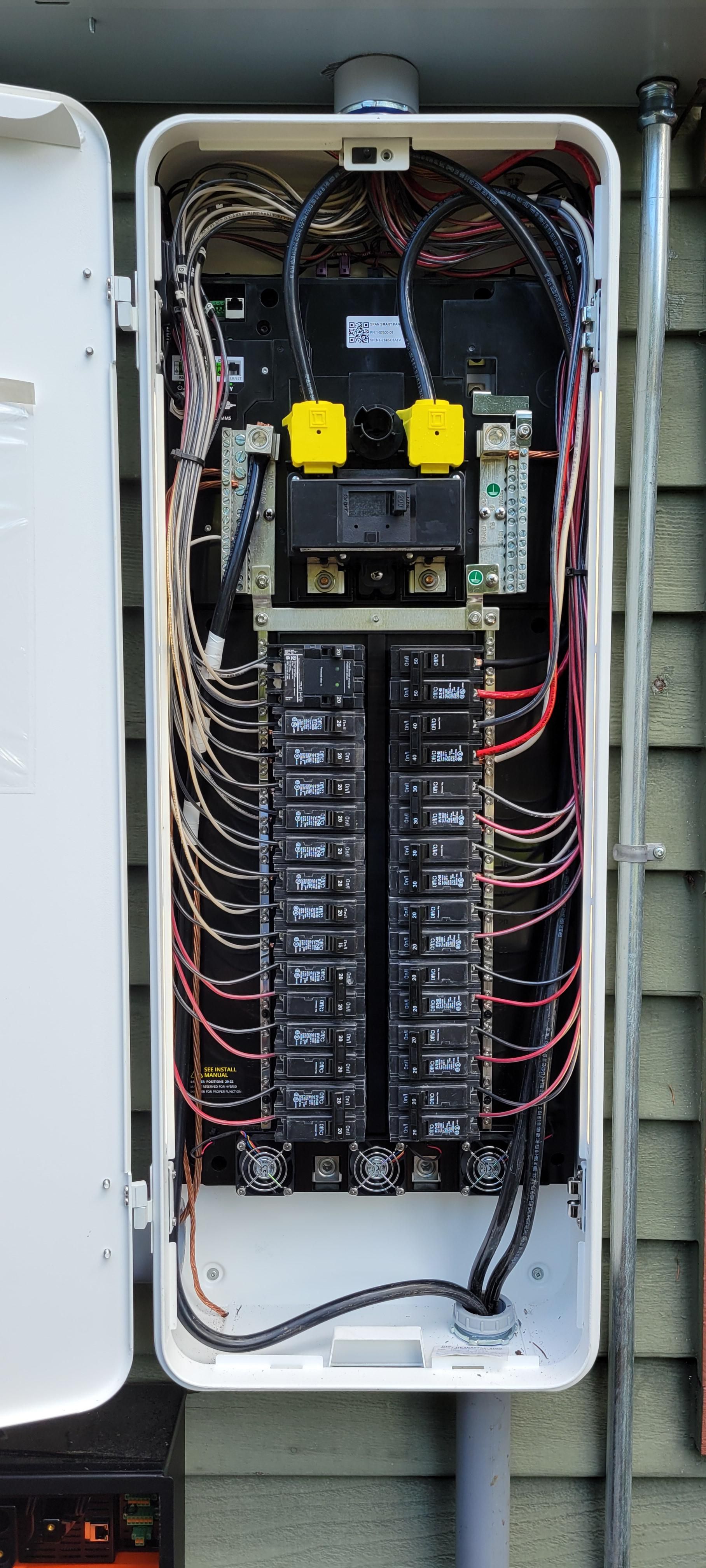 An open wall-mounted electrical distribution box with multiple circuit breakers and a tangle of exposed internal wiring.