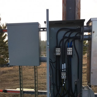 Gray electrical control boxes with wiring mounted on utility poles outdoors.