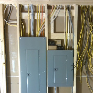 Two gray electrical breaker panels mounted between wooden wall studs with multiple yellow and gray cables connected.
