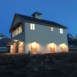 Lit barn-style house at dusk with warm porch lights and mountains in the background