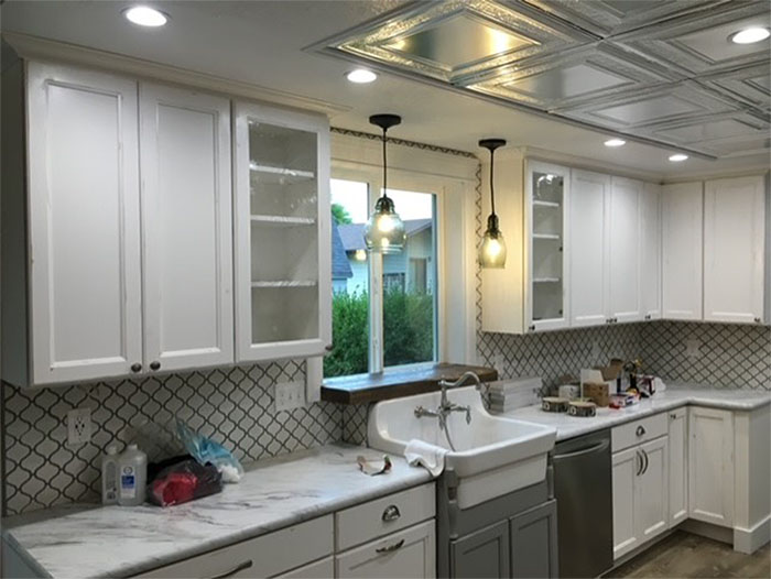 Bright white kitchen with marble counters, farmhouse sink, and pendant lights above a tiled backsplash.