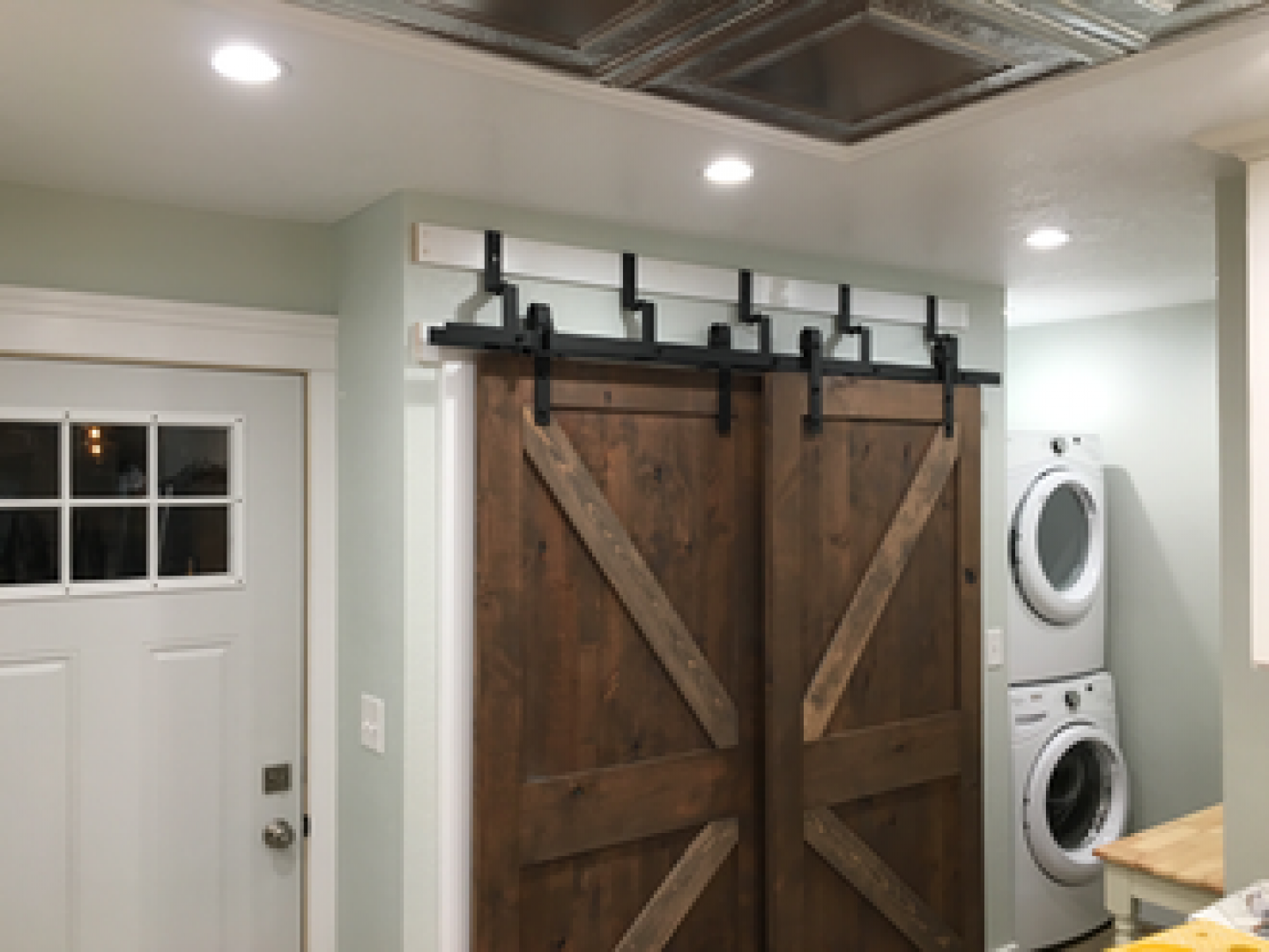 Laundry room with a barn-style sliding door, white side door, and stacked washer and dryer.