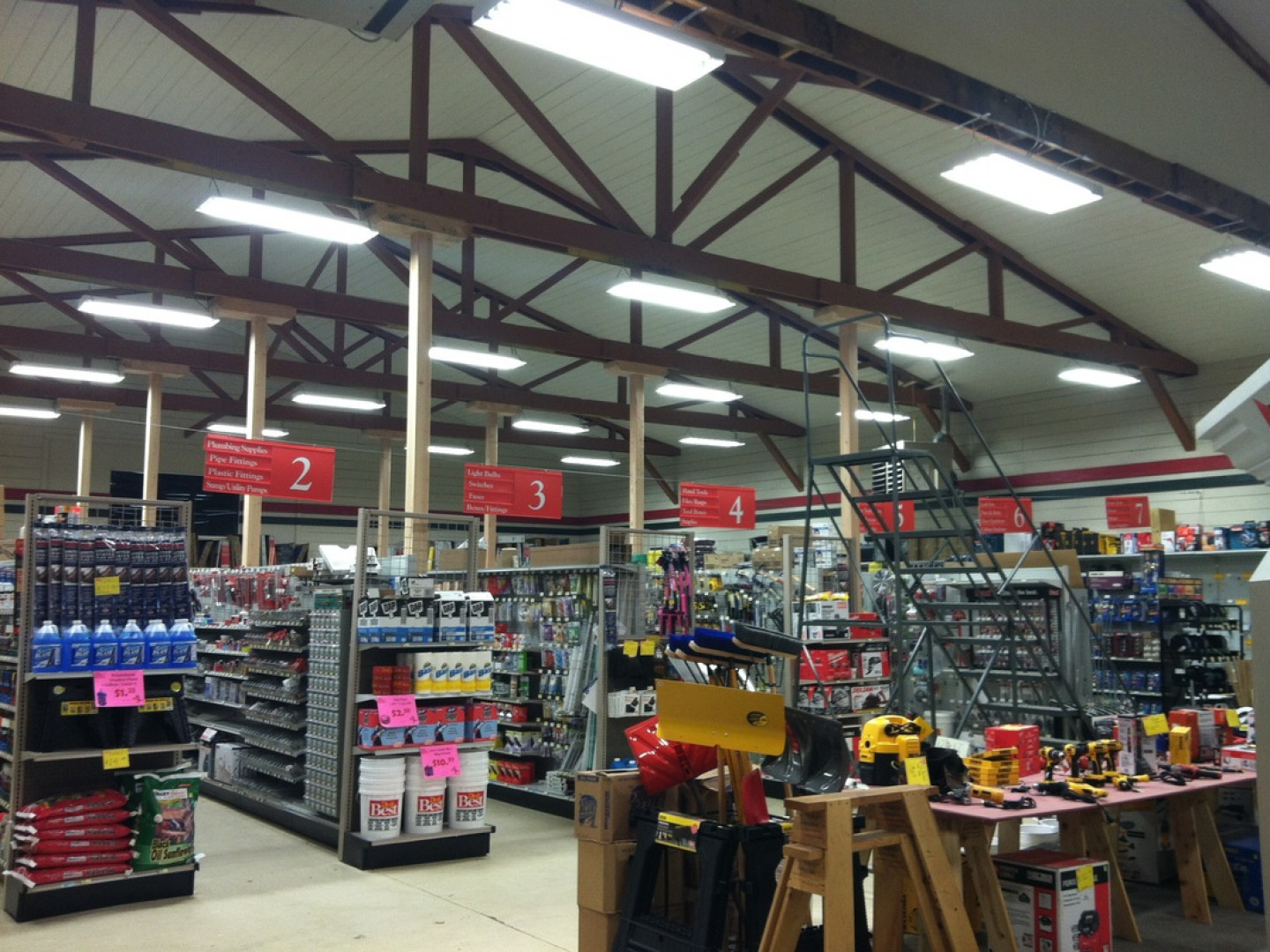 Hardware store interior with aisles of tools, shelves, and overhead signs under a high ceiling