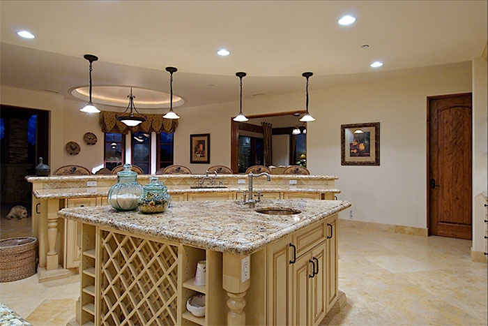 Spacious beige kitchen with granite island, pendant lights, and decorative vases
