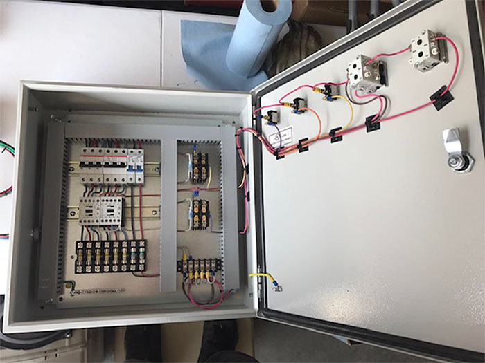 An open gray metal electrical enclosure with circuit breakers, terminal blocks, and wired components mounted inside.