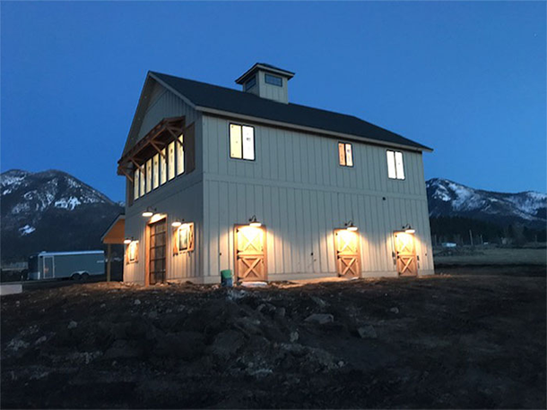Two-story white barn-style house lit at dusk, with mountains in the background.