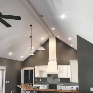 A kitchen with white cabinets, dark countertops, a vaulted ceiling, pendant lighting, and dark grey walls.