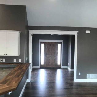 A hallway with dark grey walls and dark wood floors leading to a wooden front door with side windows.