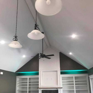 A vaulted living room features a fireplace flanked by built-in shelves, pendant lights, and glowing teal ambient lighting.