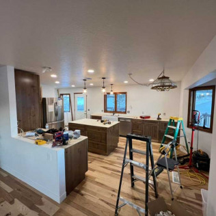 A kitchen under renovation with dark wood cabinets, a central island, new wood flooring, and ladders on the floor.