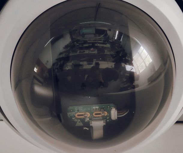 A white dome security camera mounted on a ceiling, capturing a reflection of an office space in its glass lens.