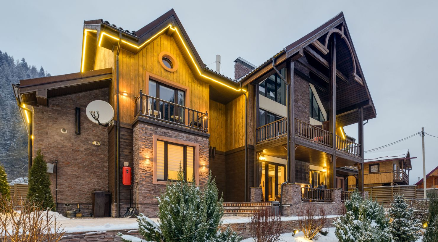 Snowy mountain lodge with warm lights and evergreen shrubs at dusk