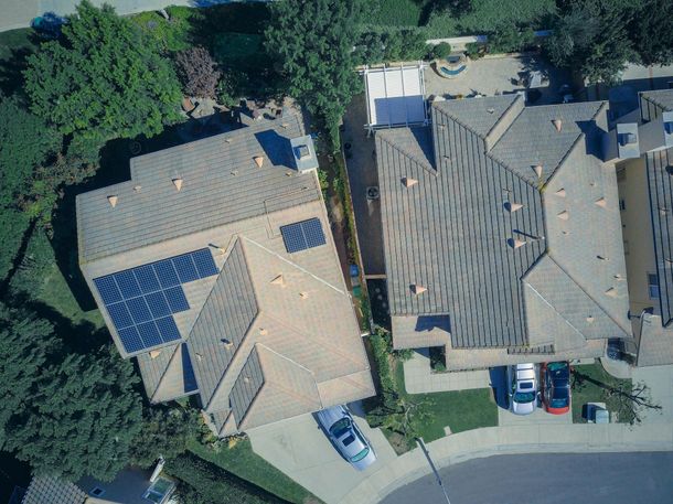 An aerial view of two residential houses, one with rooftop solar panels and two cars parked in the driveways.
