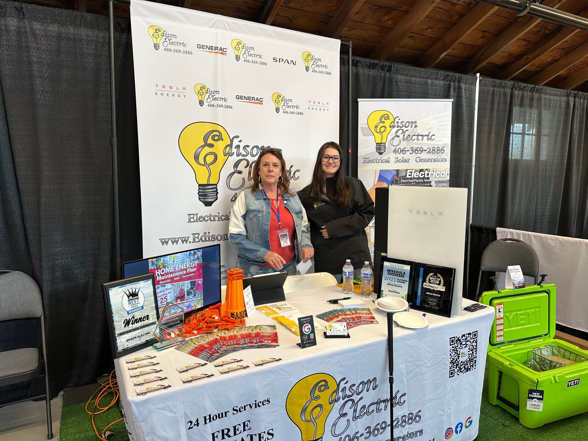 Booth at a trade show with two people standing behind a table of promotional items and banners
