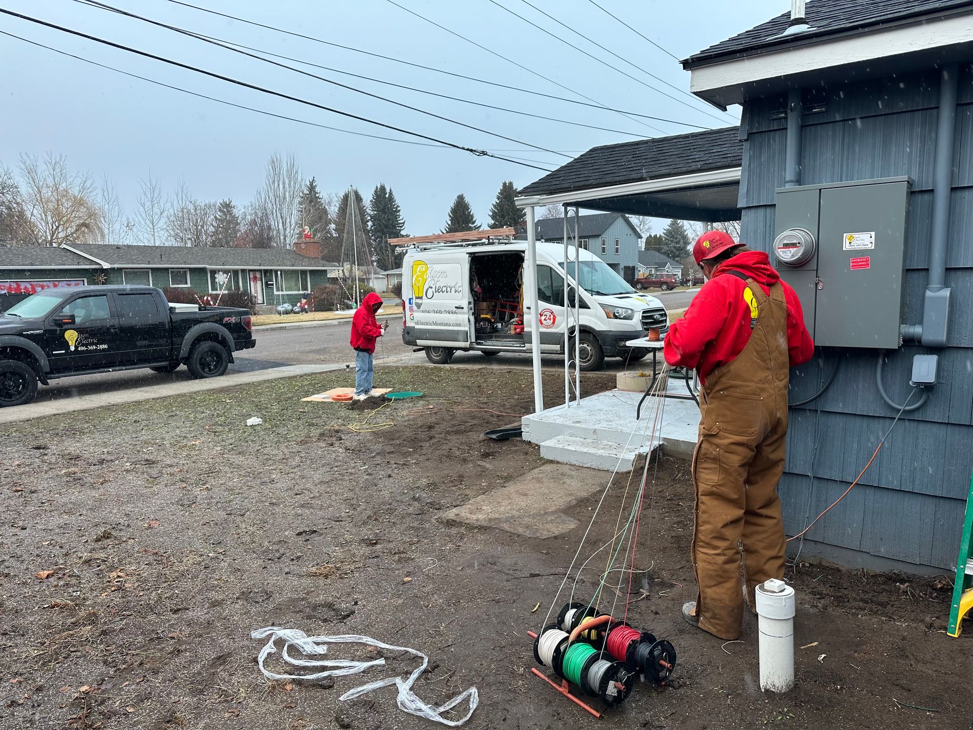 Worker in red jacket and brown overalls washing equipment beside a building, with a truck nearby.