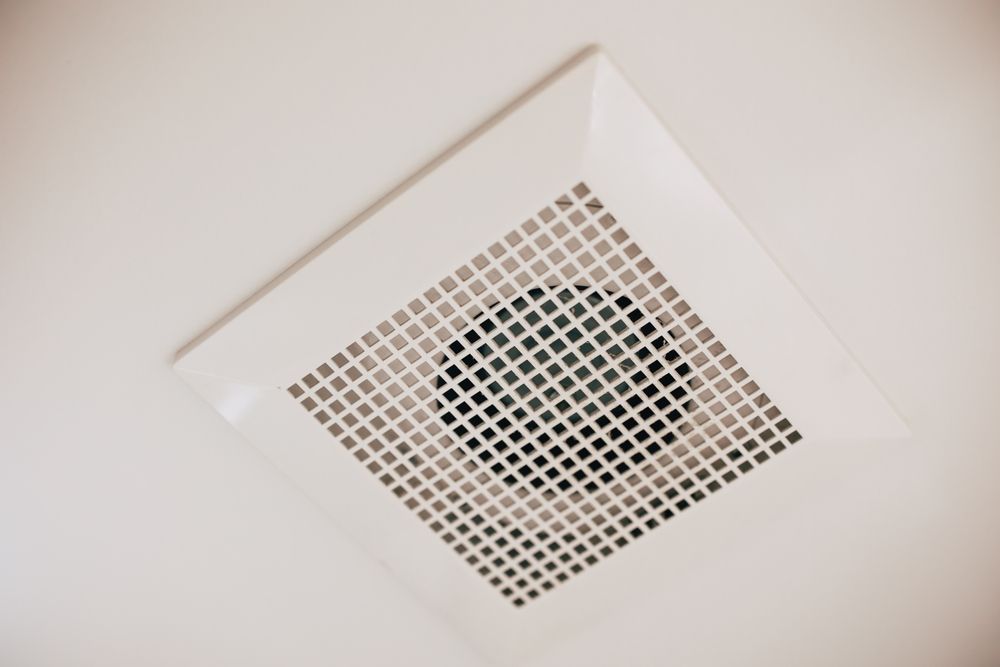 White ceiling ventilation grille with a dark circular fan or vent in the center